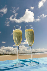 Close-up of champagne flutes on beach against sky