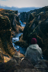 Rear view of woman sitting on rock looking at view