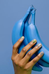 Close-up of woman hand holding artificial bananas against blue background