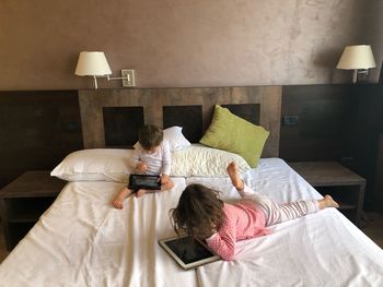 High angle view of siblings with technology lying on bed at home