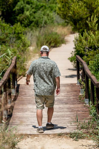 A person walking on wooden walkway in nature. man in casual clothing trekking in park. summer wear.