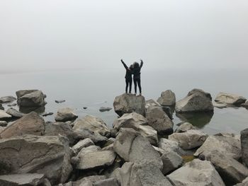 People standing on rock at beach against sky