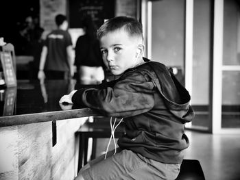 Portrait of boy listening to music while sitting by table in restaurant
