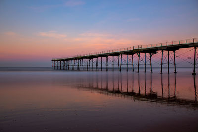 Silhouette bridge over sea against sky during sunset