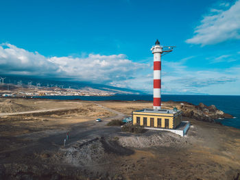 Lighthouse amidst sea and buildings against sky