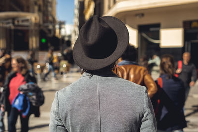 Rear view of man standing on street in city during sunny day