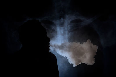Portrait of smoke emitting from silhouette man against black background