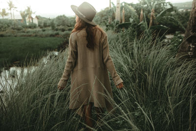 Rear view of woman walking amidst grassy field by lake at forest