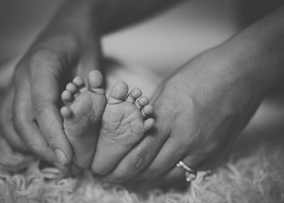 Close-up of hand holding baby feet on bed
