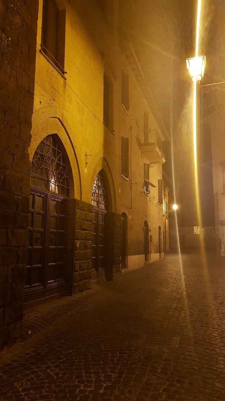 ILLUMINATED STREET LIGHTS ON FOOTPATH AMIDST BUILDINGS IN CITY