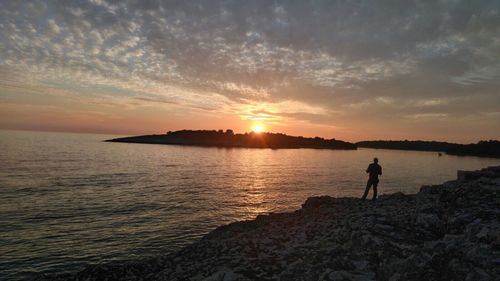 Silhouette man standing on beach against sky during sunset