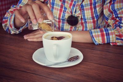 Midsection of woman adding brown sugar in coffee at table