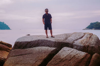 Man standing on rocky shore against cloudy sky