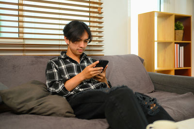 Young man using phone while sitting on sofa at home