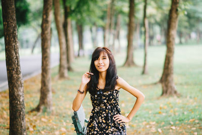 Portrait of young woman standing by tree trunk in forest