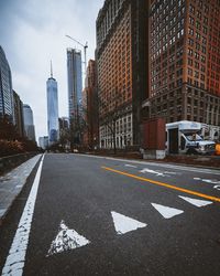 Empty road in city against cloudy sky