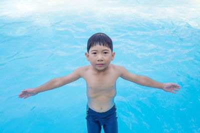 Portrait of shirtless boy with arms outstretched in swimming pool