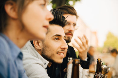 Smiling man sitting by male and female friend at social gathering