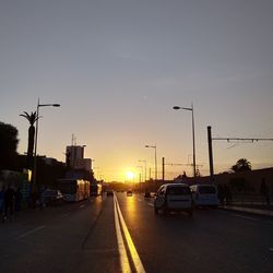 Cars on city street against sky during sunset