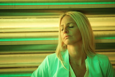 Close-up of woman with eyes closed against illuminated shutter