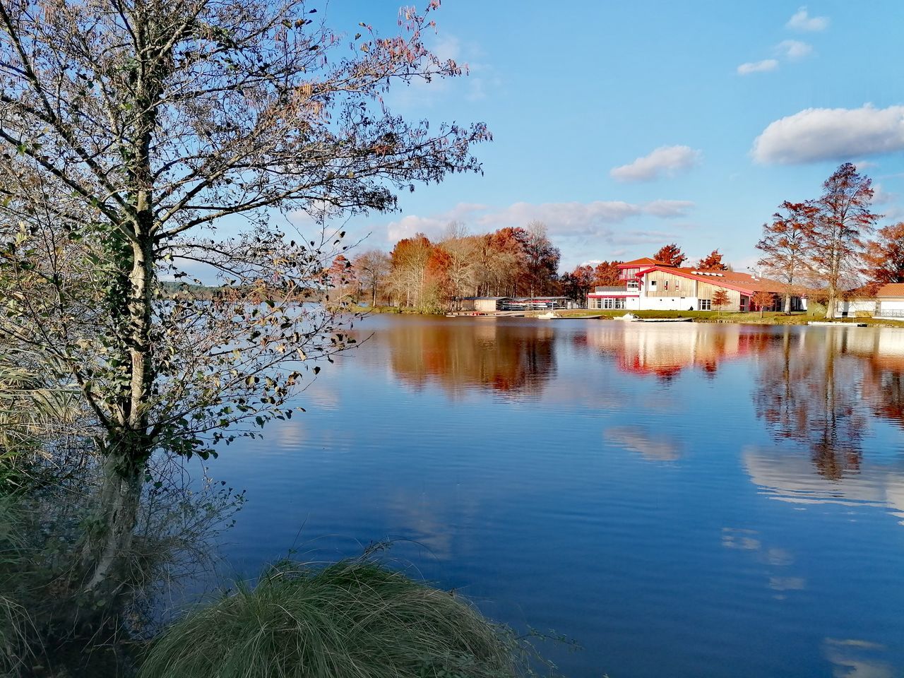 water, tree, reflection, plant, sky, nature, autumn, lake, architecture, beauty in nature, scenics - nature, built structure, tranquility, no people, flower, cloud, building exterior, travel destinations, landscape, blue, tranquil scene, leaf, morning, building, outdoors, day, house, body of water, idyllic, travel, environment, tourism