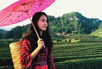 Side view of woman wearing traditional clothing holding umbrella standing against sky