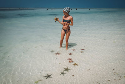 Woman holding starfishes while standing on shore at beach