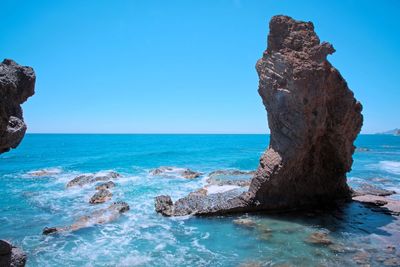 Rock formation in sea against clear blue sky