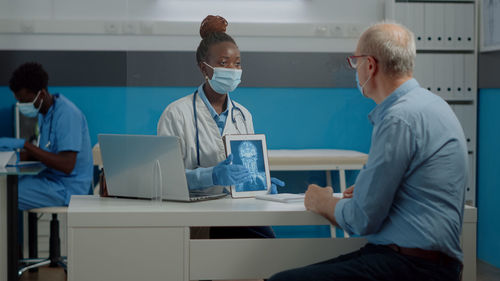 Doctor wearing mask showing medical xray in tablet to patient in clinic