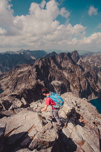 Young man climbing mountain against cloudy sky