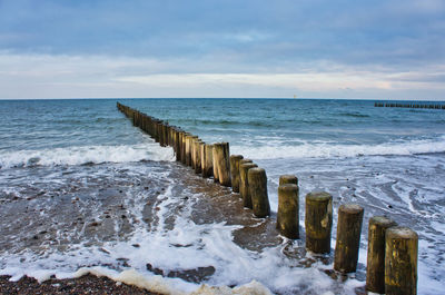 Wooden posts on sea against sky