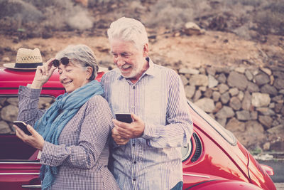 Senior couple using smart phones while standing by car