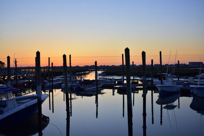 Sailboats moored in harbor at sunset