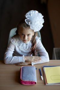 Portrait of cute girl sitting with pouch and files on table