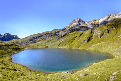 Scenic view of lake and mountains against clear blue sky