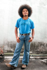 Man with round black frizzy hair, dressed in a blue shirt and long pants