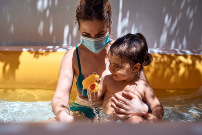 Young mother with a mask in an inflatable pool with her little daughter. safe holiday concept