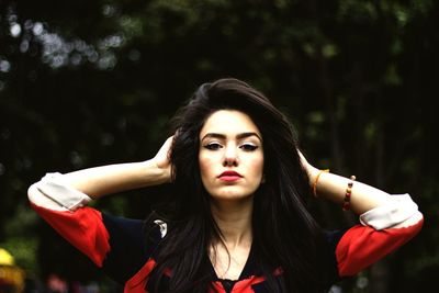 Portrait of beautiful woman with hand in hair standing against trees at park