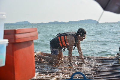 Side view of man kneeling on wooden raft in sea