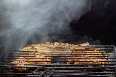 Smoke rising from roast meat on open barbecue.