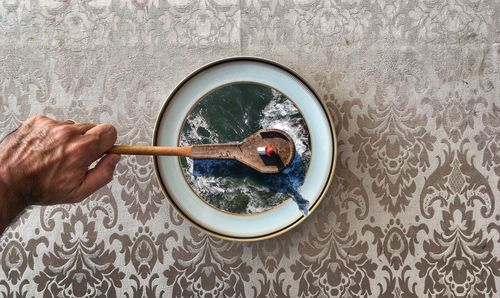 Directly above shot of cropped hand holding spoon over plate with waves art