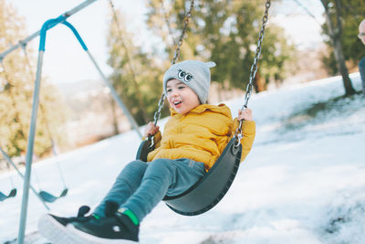 Full length of happy boy playing on swing in playground