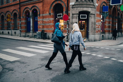 Full length of smiling young muslim women walking on street in city