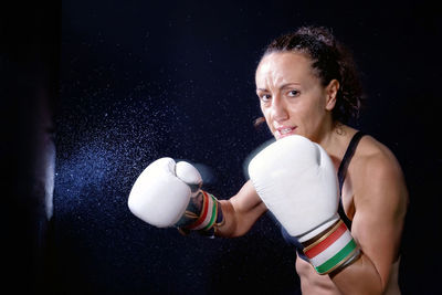 Portrait of woman practicing boxing against black background