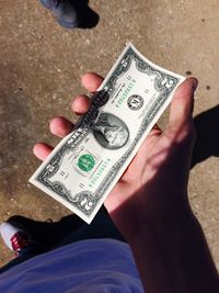 Low section of man holding paper currency on street during sunny day