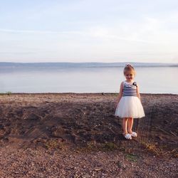 Portrait of smiling girl standing at lakeshore against sky