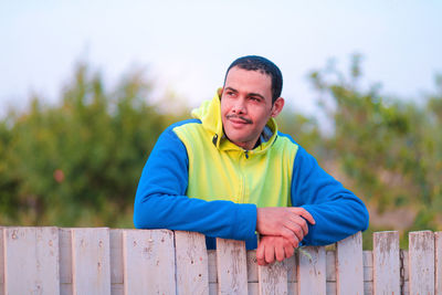 Portrait of young man standing against fence