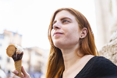 Relaxed ginger woman with ice cream cone in city