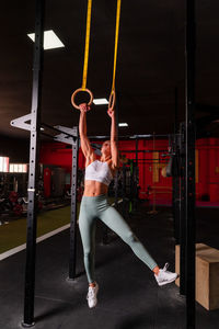 Muscular female athlete in sportswear hanging on gymnastic rings and doing exercises for abs in contemporary fitness center