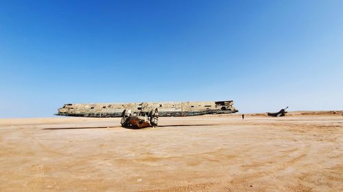 Damaged airplane on desert against clear blue sky